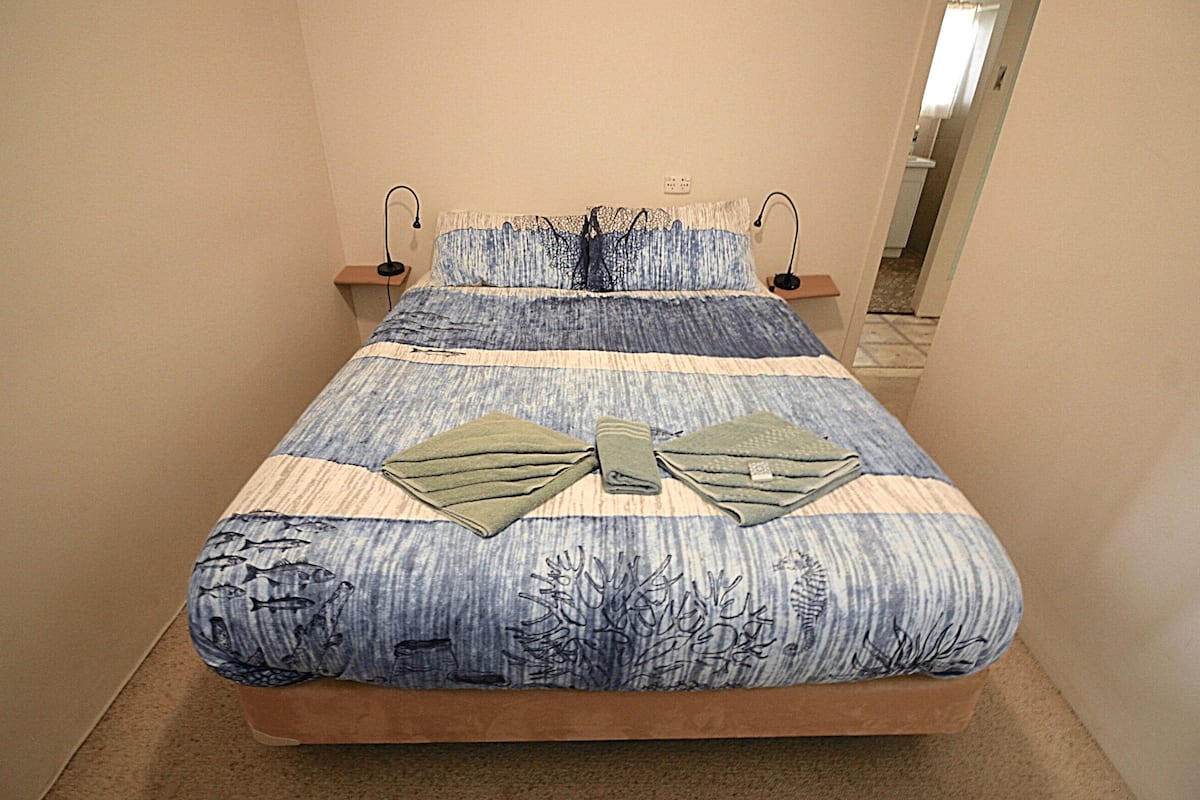 Una cama con una colcha a rayas azules y blancas, dos almohadas y dos lámparas de noche.