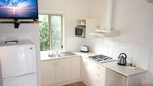 Une cuisine moderne avec des armoires blanches, un four à micro-ondes encastré, une cuisinière à gaz et un téléviseur à écran plat fixé au-dessus du réfrigérateur.