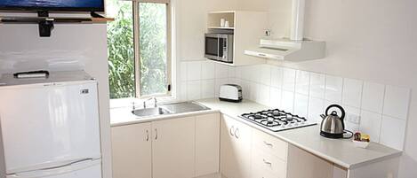 A modern kitchen with white cabinets, a built-in microwave, a gas stove, and a flat-screen TV mounted above the refrigerator.