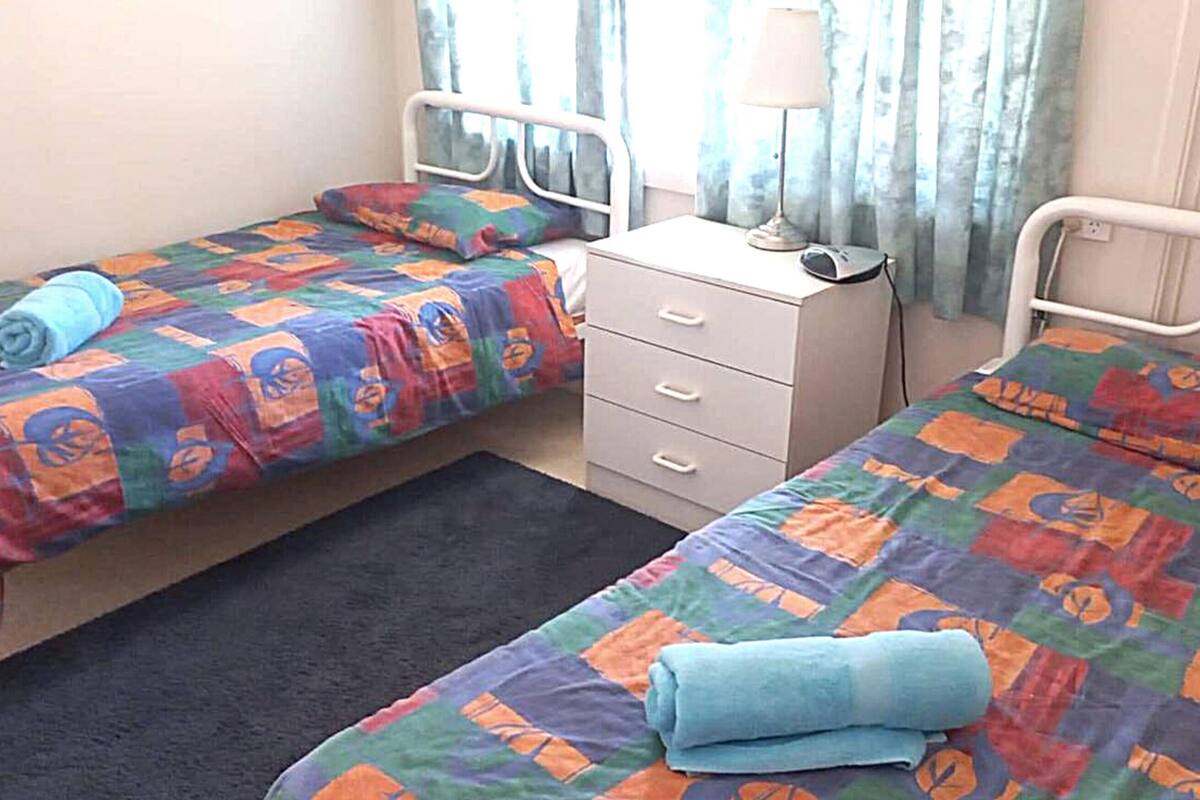 Un dormitorio con dos camas, cada una con ropa de cama y un cojín de colores. Hay una mesita de noche con una lámpara y un teléfono.