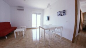 A spacious living area with a red sofa, white tables, and chairs, a TV mounted on the wall, and a sliding glass door leading to a balcony. - Apartamentos H3 Laguna Playa (Roquetas de Mar)