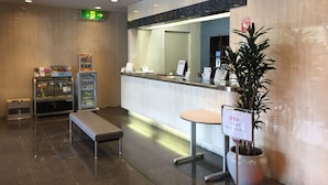 Un área de recepción con mostrador, banco, planta y máquina expendedora.