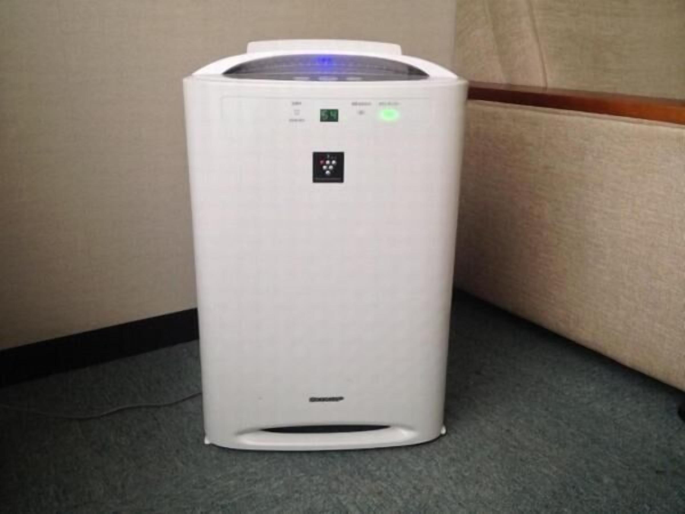 A white portable heater with a digital display and control buttons, placed on a carpeted floor.