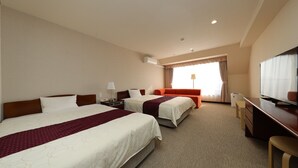 Habitación de hotel con dos camas, un escritorio, televisor y ventana con cortinas.