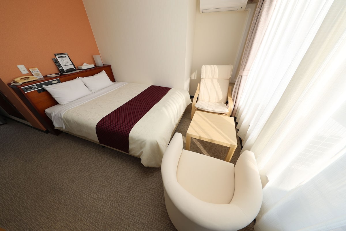 Ett hotellrum med en säng, en stol, ett litet bord och en telefon.
