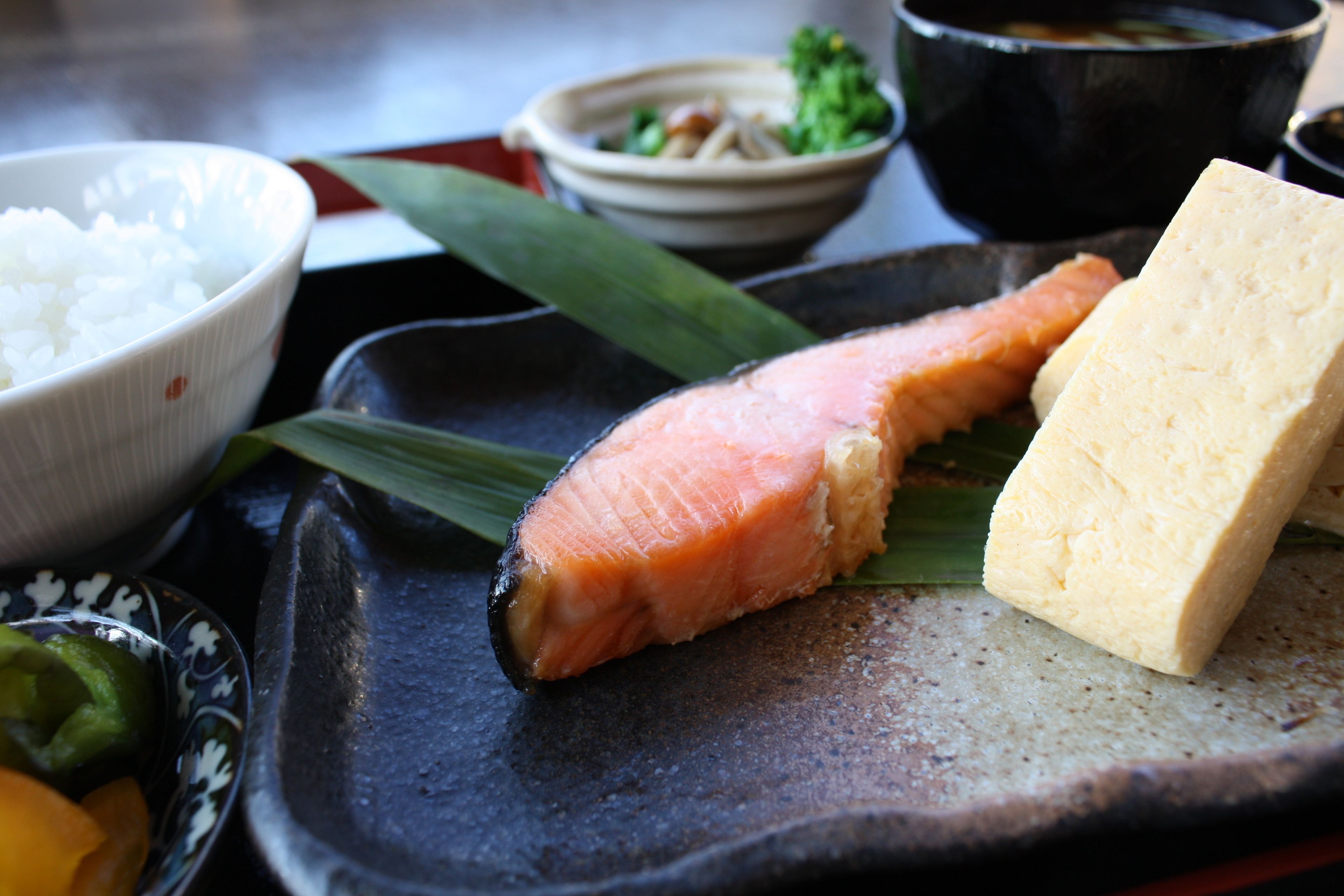 A traditional Japanese meal with salmon, tofu, rice, and pickled vegetables on a ceramic plate.