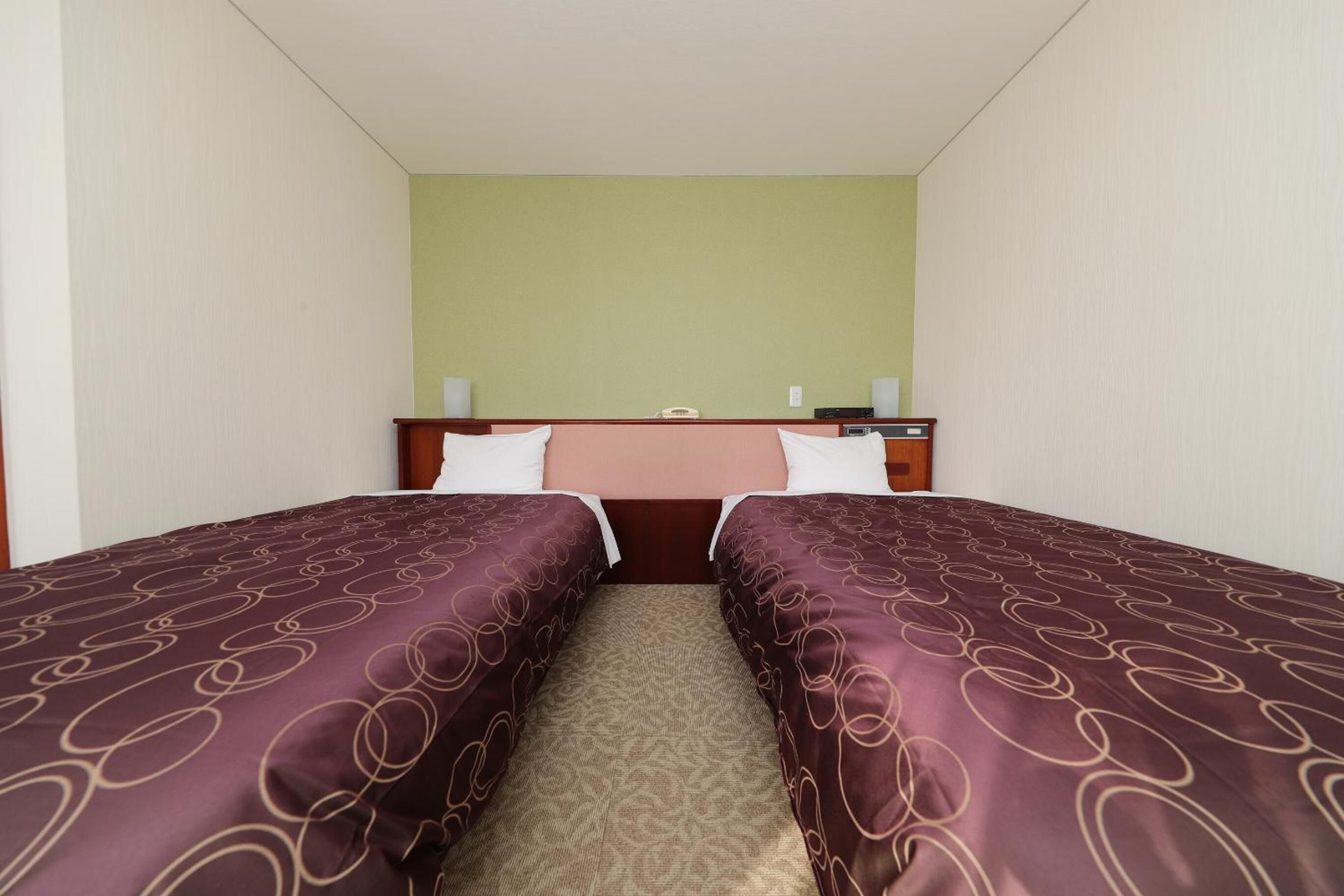 A hotel room with two single beds, a nightstand with a lamp, and a green wall.