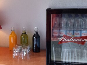 A refrigerator stocked with Budweiser bottles and several empty bottles on a counter.