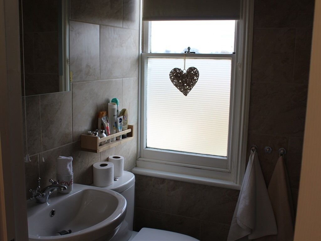 A bathroom with a sink, toilet, and window with a heart-shaped decoration.