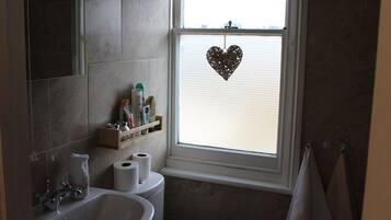 Un baño con lavamanos, inodoro y ventana decorada con un corazón.