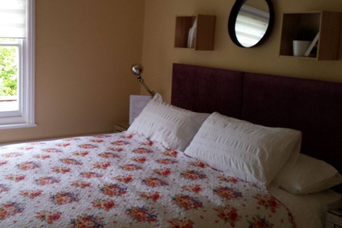 A bedroom with a bed, a window, a mirror, and a bedside table.