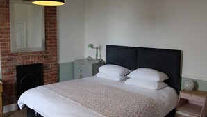 Une chambre à coucher avec un lit, une table de chevet, une lampe, une commode et un mur en briques.
