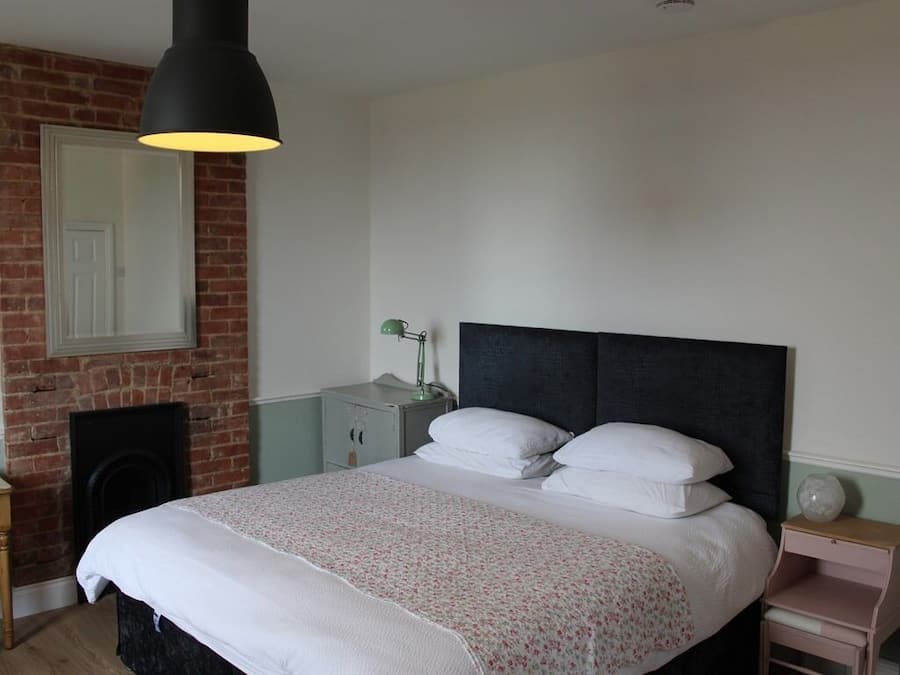 A bedroom with a bed, a nightstand, a lamp, a dresser, and a brick wall.