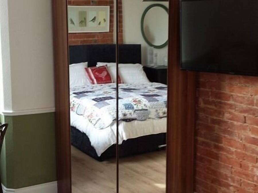 Un dormitorio con cama, espejo, televisor y pared de ladrillo.