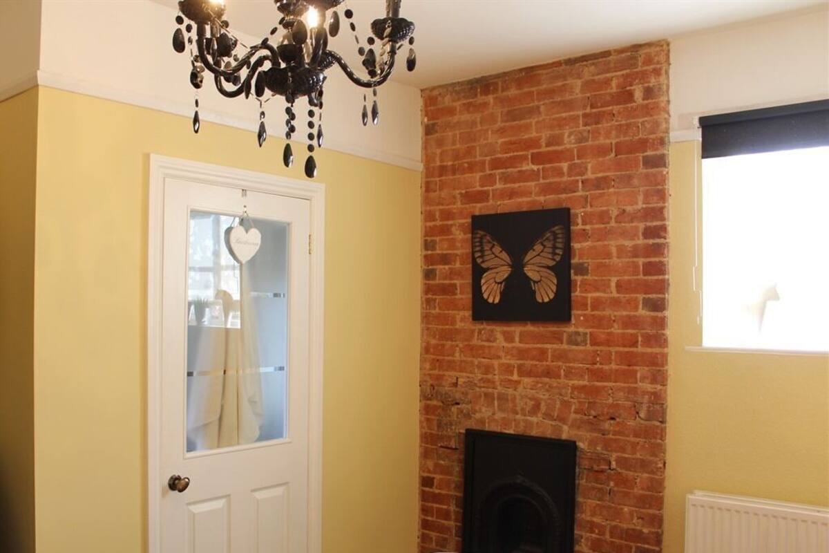 A room with a brick fireplace, a chandelier, a door with a heart-shaped decoration, and a butterfly wall art piece.