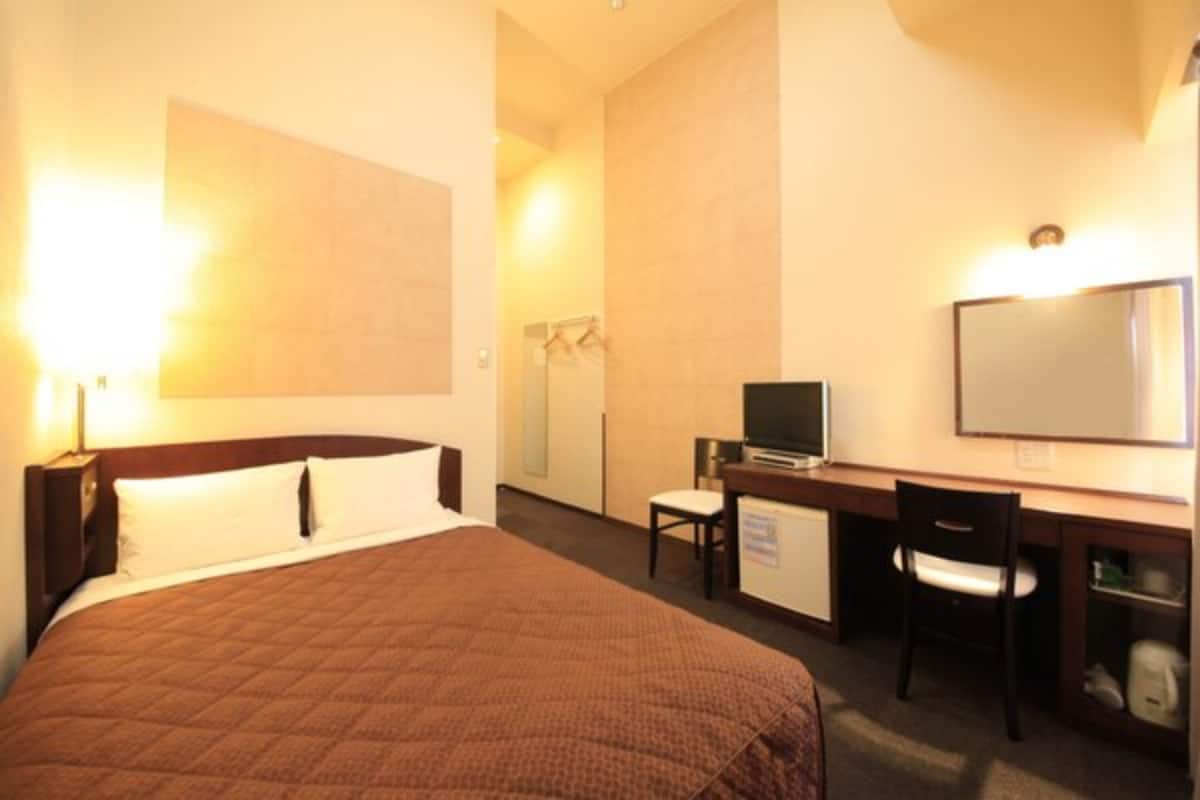 A hotel room with a large bed, a desk with a chair, a television, and a mirror.