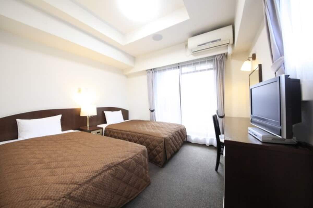 A hotel room with two beds, a desk with a television, and a window with curtains.