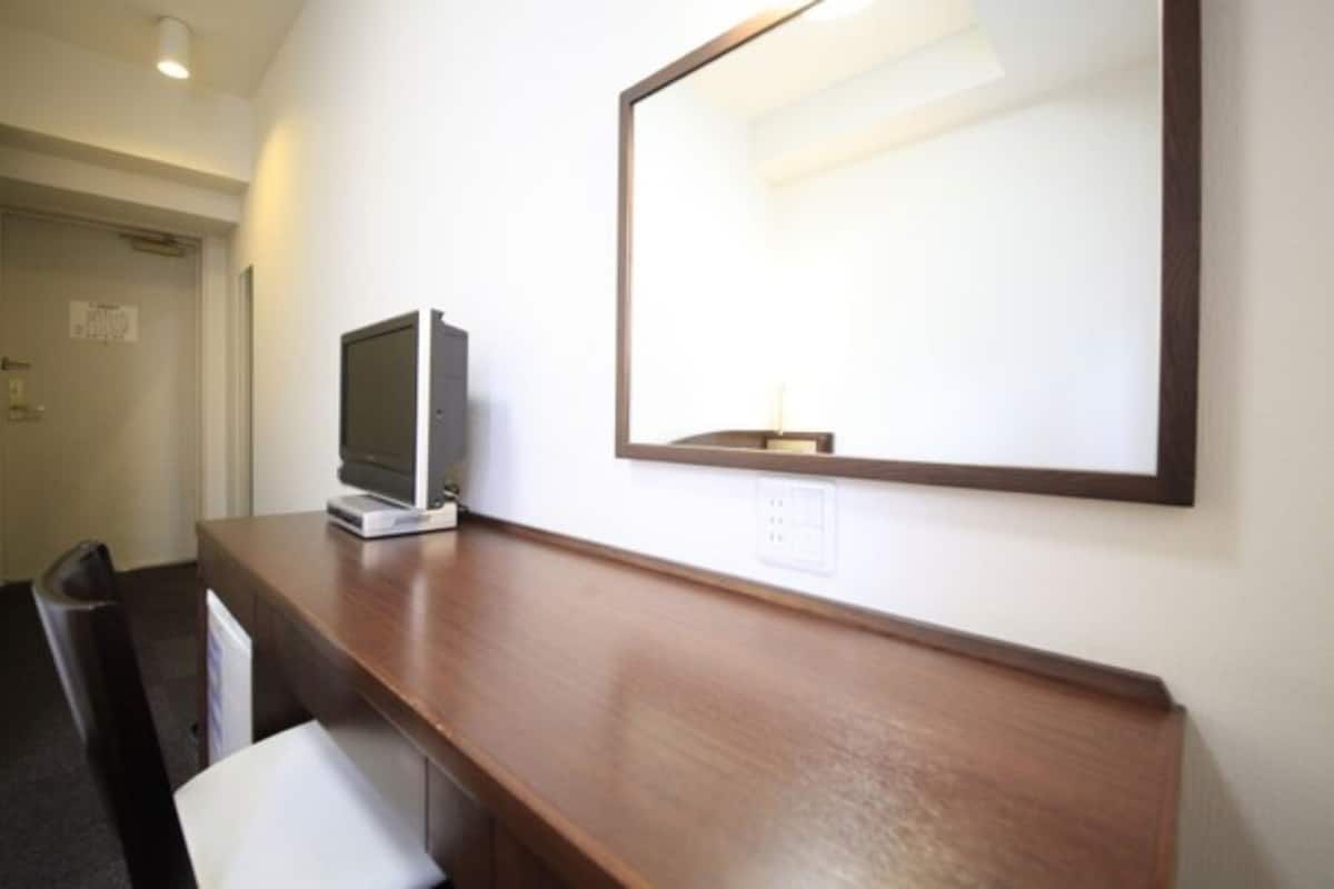 A hotel room with a wooden desk, a television, and a large mirror on the wall.