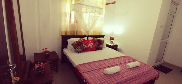 A bedroom with a bed, bedside table, lamp, and a window with curtains.