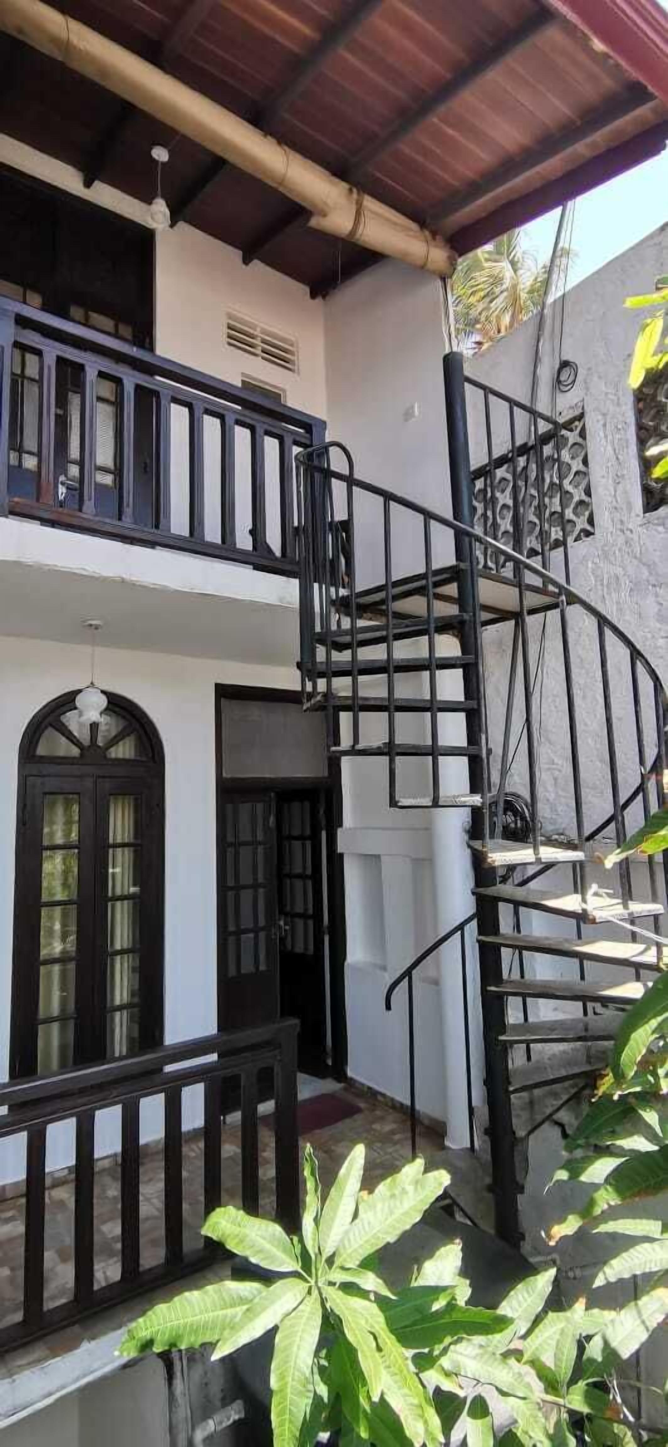 Un edificio de dos pisos con una escalera en espiral, un balcón y una puerta con paneles de vidrio.