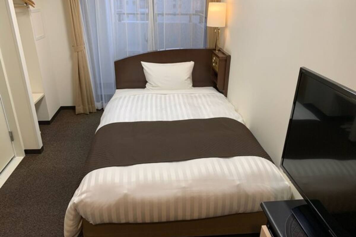 A hotel room with a bed, a television, and a window with curtains.