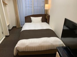 Quarto de hotel com cama, televisão e janela com cortinas.