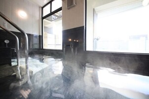 Uma sala de vapor com parede de vidro, corrimão metálico e piso ladrilhado.