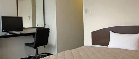 A hotel room with a bed, a desk with a computer and monitor, a chair, and a large mirror.