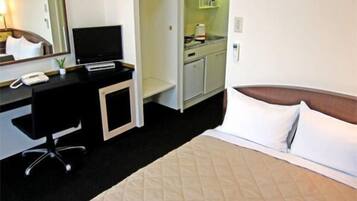 Une chambre d’hôtel comprenant un lit, un bureau avec un téléphone, une télévision et une kitchenette.