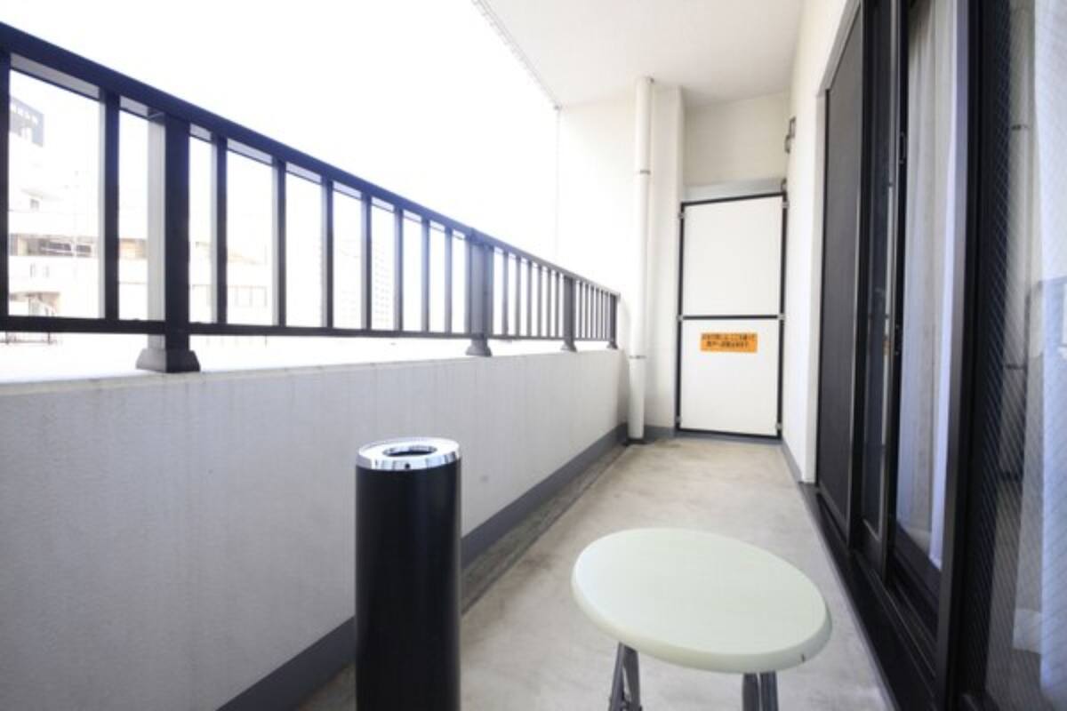 A narrow corridor with a white wall, a black trash bin, and a small white table.