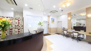 A reception area with a curved reception desk, a whiteboard, and a seating area with chairs and a table. - Tachikawa Urban Hotel Annex (Tachikawa)