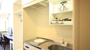 A compact kitchenette with a built-in stove, sink, and shelves for storage. - Tachikawa Urban Hotel Annex (Tachikawa)