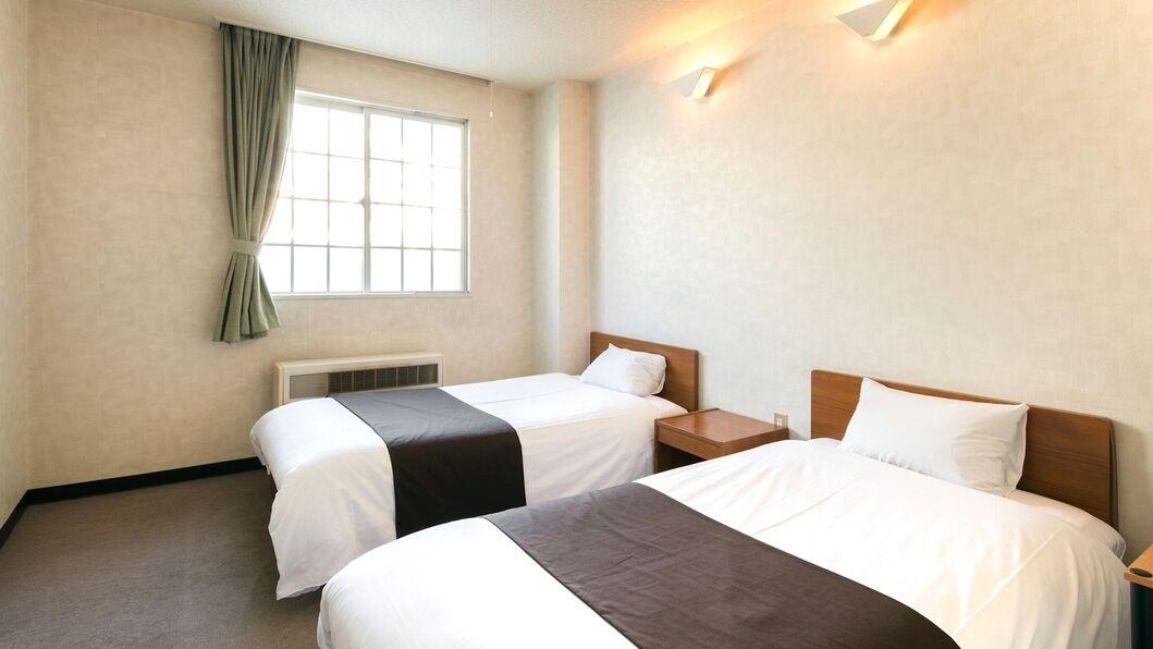 Quarto de hotel com duas camas, uma janela com cortinas, um radiador e uma mesa de cabeceira.