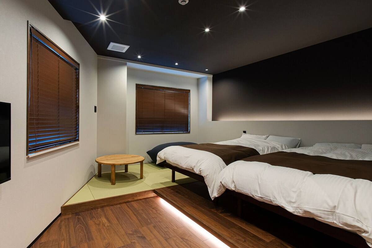 A modern bedroom with a TV, two beds, a small table, and wooden flooring.