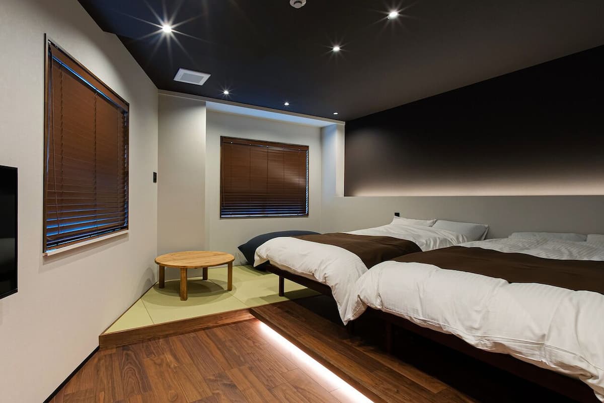 A modern bedroom with a TV, two beds, a small table, and wooden flooring.