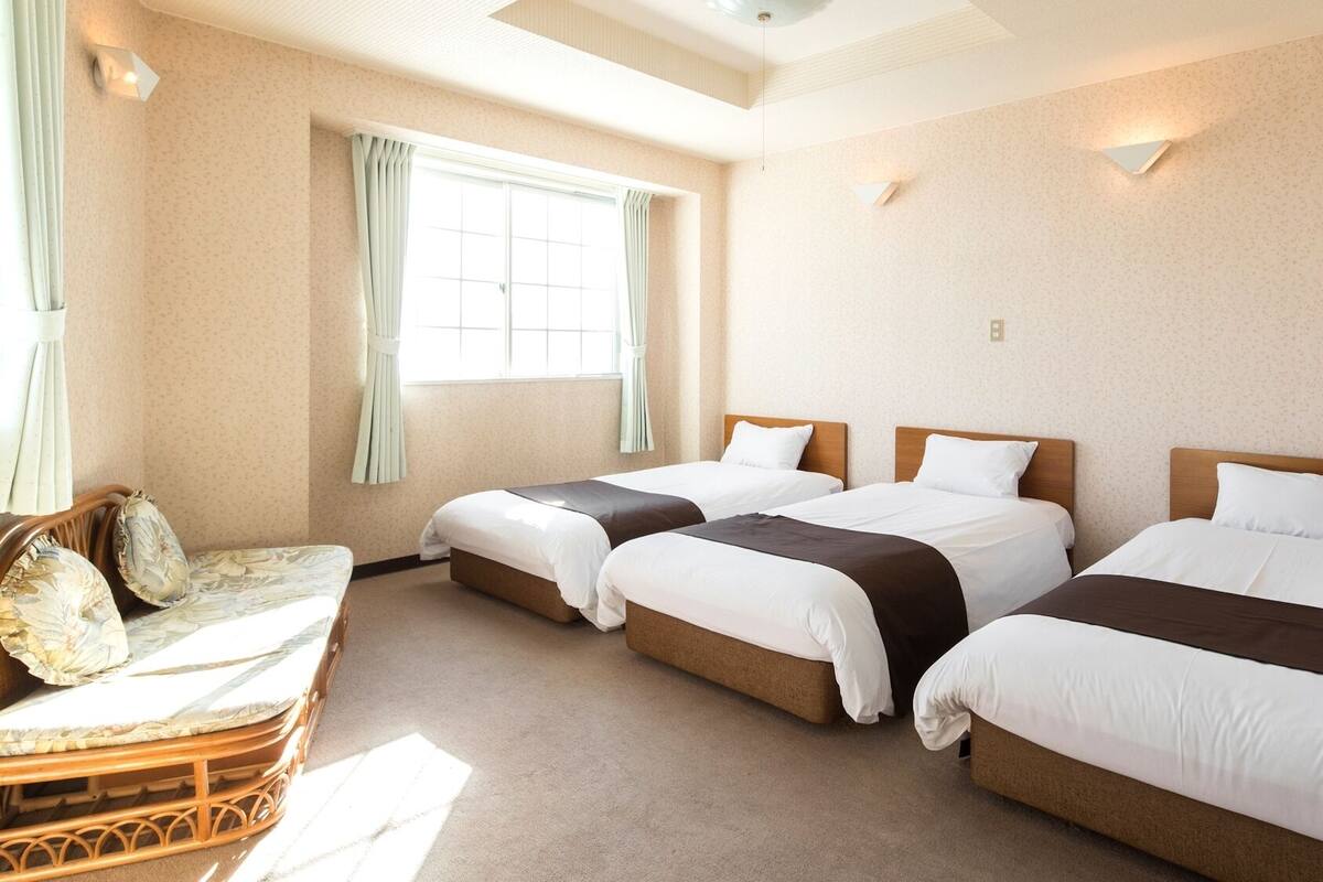 A hotel room with three beds, a small seating area, and a window with curtains.