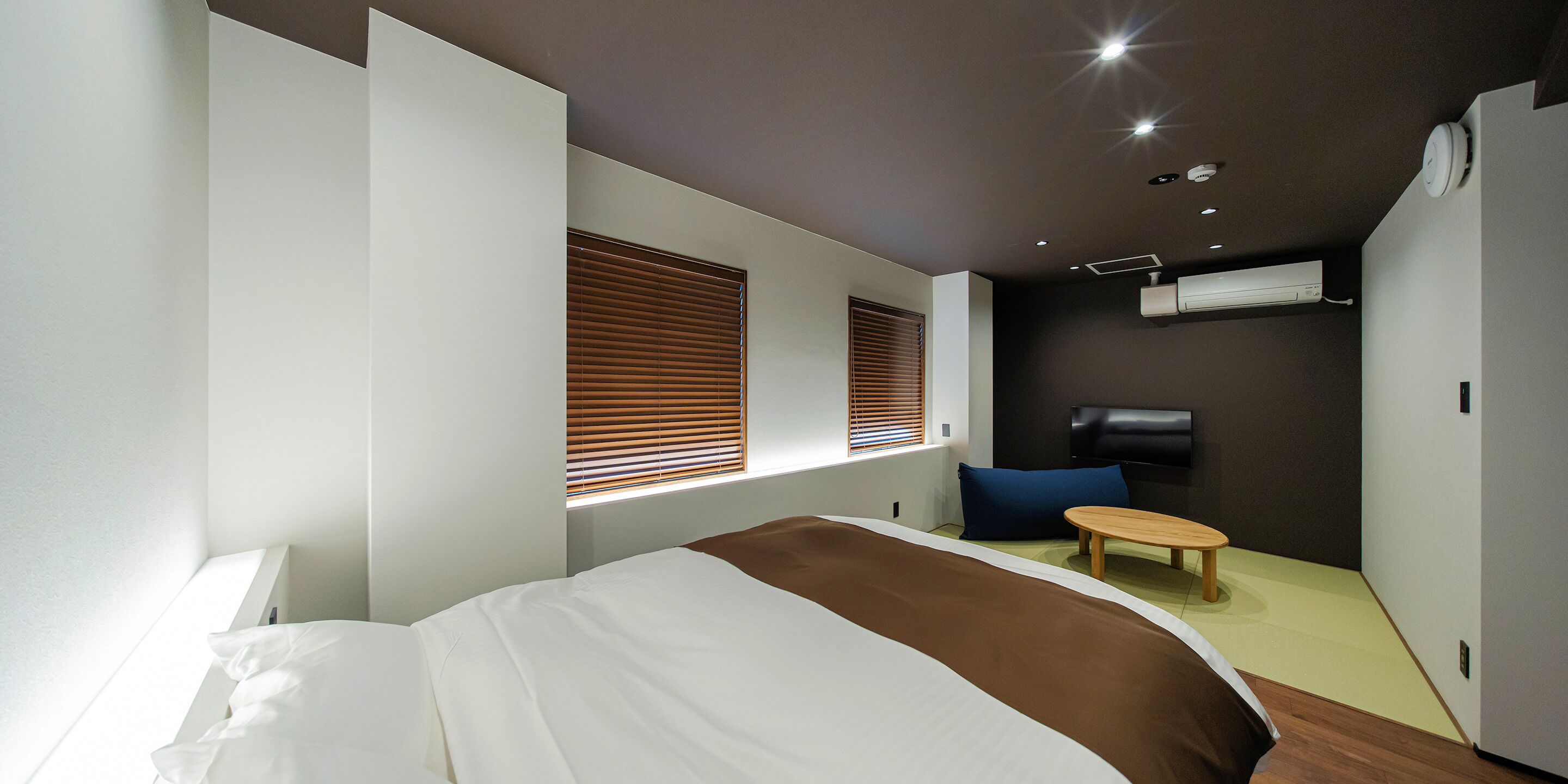Una habitación de hotel moderna con una cama grande, una zona de estar pequeña, un televisor y un aire acondicionado.
