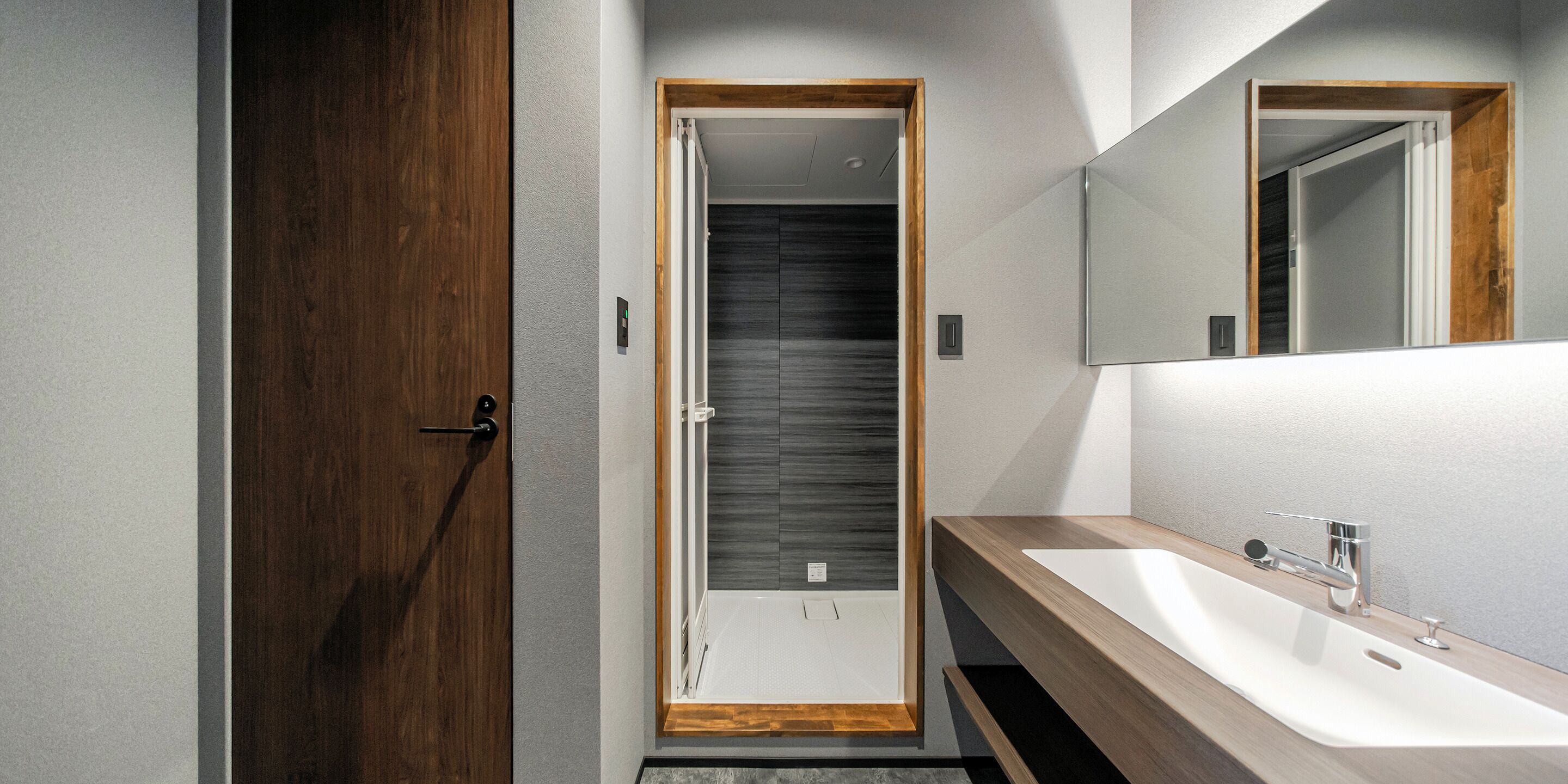 A modern bathroom with a wooden door, a large mirror, and a white sink.
