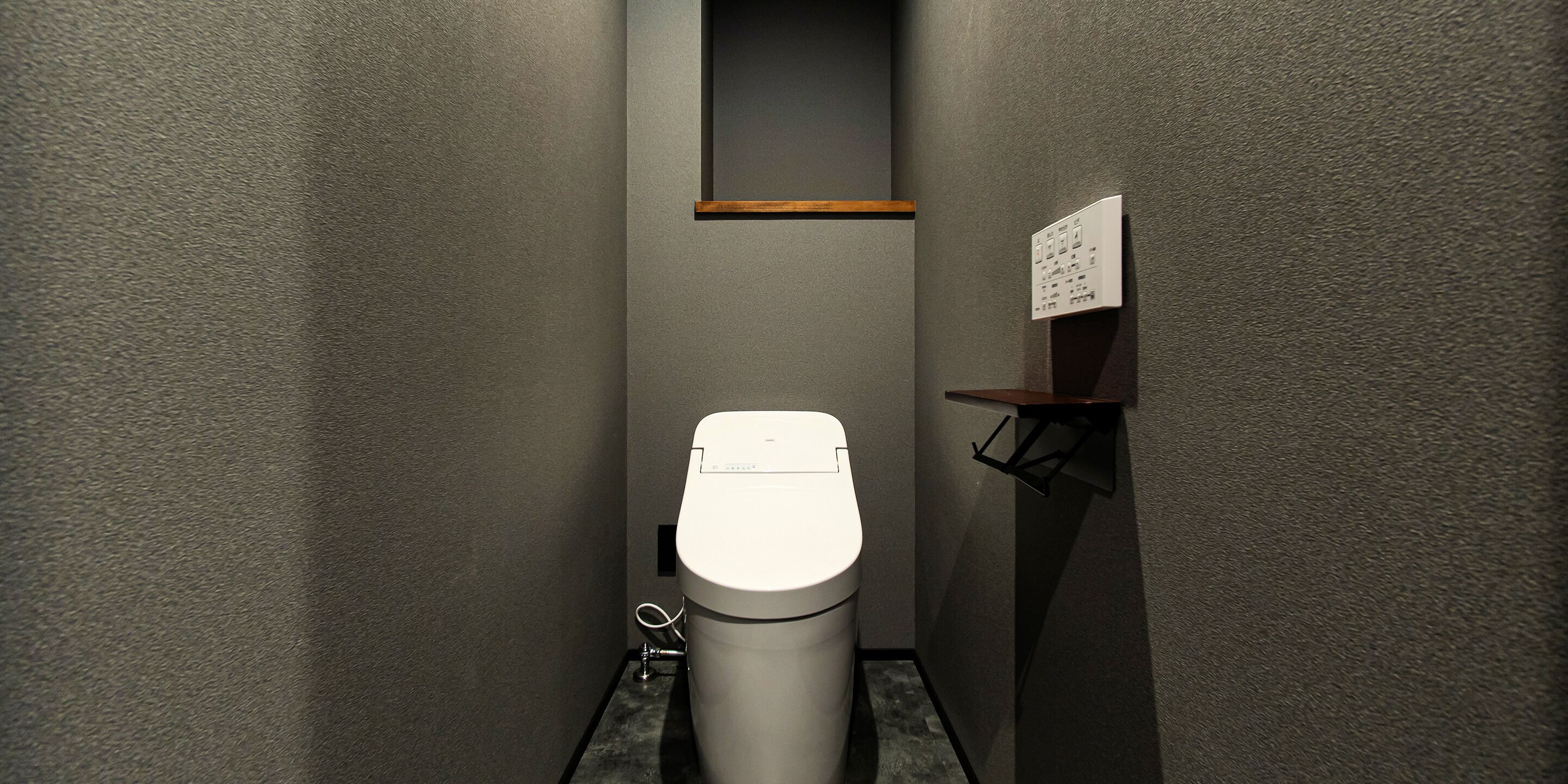Un baño moderno con inodoro, un pequeño estante con un letrero y un pulsador de descarga en la pared.