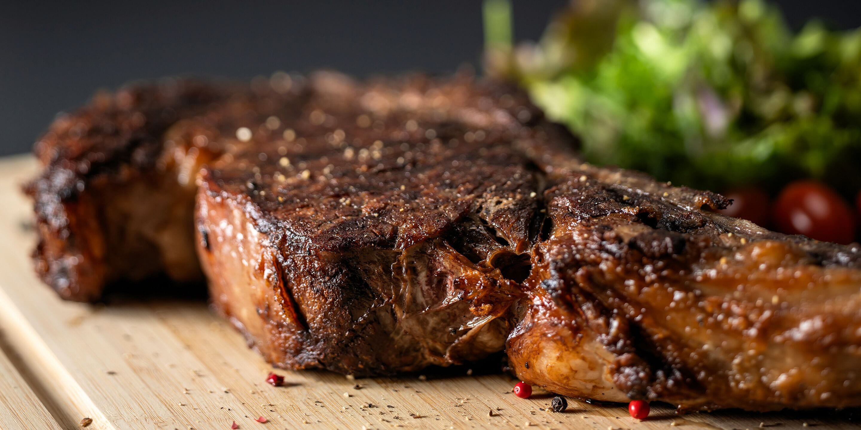 Un filete a la parrilla sobre una tabla de madera con hierbas y un recipiente pequeño de salsa.