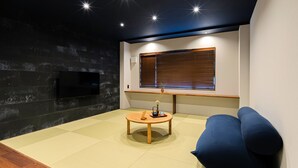 A modern living room with a dark wall, a wooden coffee table, a blue sofa, and a TV mounted on the wall. - Yunoyado Mochizuki (Myoko)
