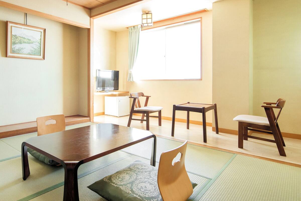 A traditional Japanese room with tatami flooring, a low table, and wooden chairs.
