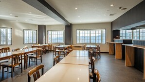 A spacious conference room with multiple tables and chairs, large windows with a view, and a kitchenette area. - Yunoyado Mochizuki (Myoko)