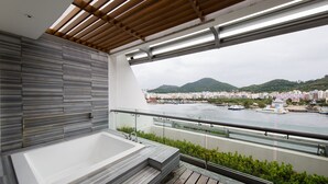 A modern balcony with a large bathtub, a wooden deck, and a view of a cityscape and mountains. - Sanya Visun Royal Yacht Hotel (Sanya)
