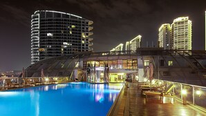 A swimming pool with sun loungers and a covered deck area, surrounded by high-rise buildings at night. - Sanya Visun Royal Yacht Hotel (Sanya)