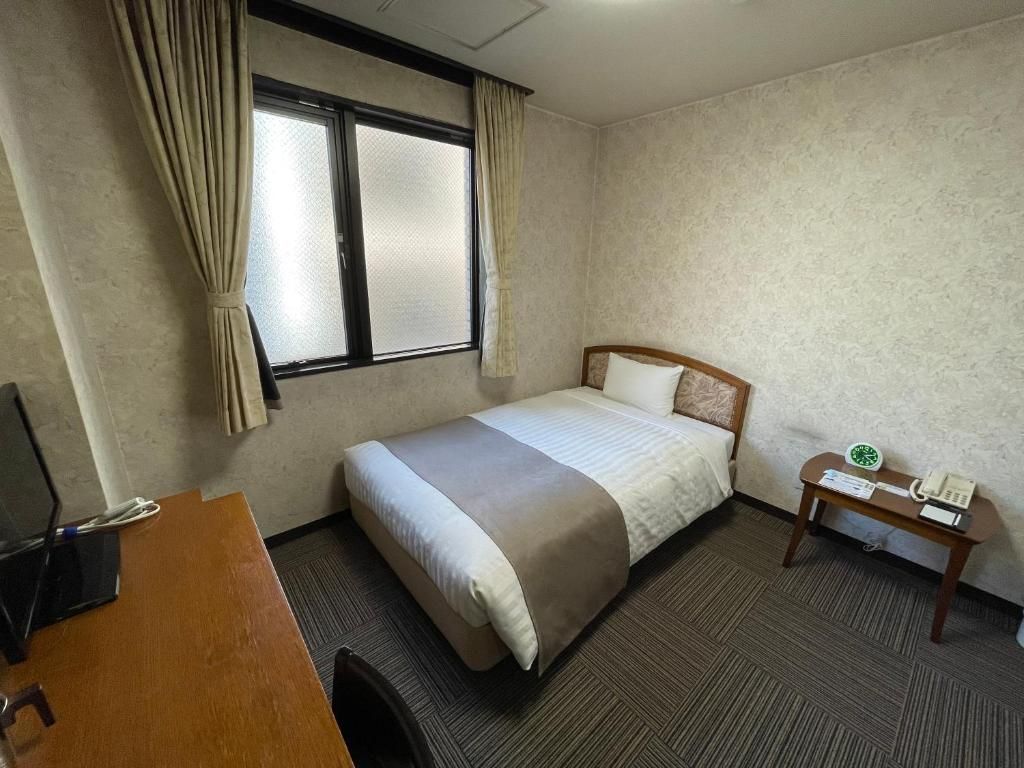 A hotel room with a bed, a desk, a telephone, and a window with curtains.
