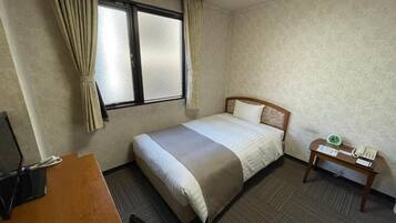 A hotel room with a bed, a desk, a telephone, and a window with curtains.