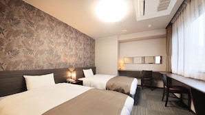 Une chambre d’hôtel avec deux lits, un bureau et une chaise. Il y a un grand miroir au-dessus du bureau et une fenêtre avec des rideaux.