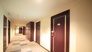 Un couloir d’hôtel avec un tapis à carreaux, des portes en bois et un mur de couleur claire.