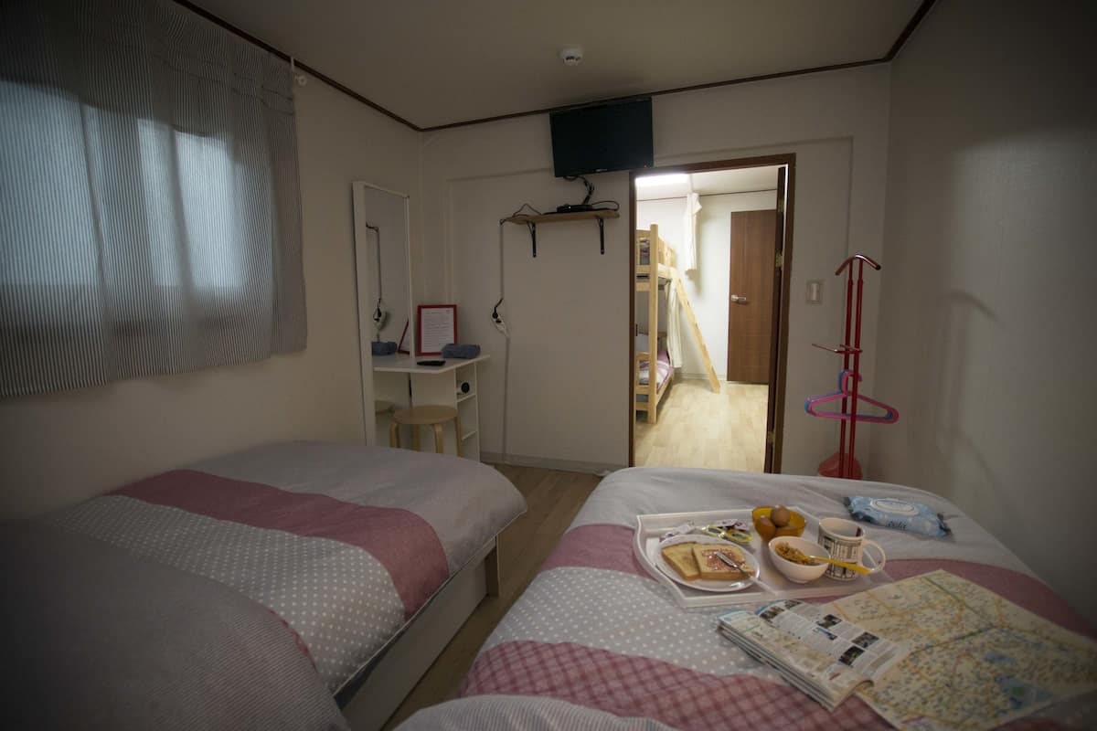 A bedroom with two beds, a desk, a television, and a door leading to a bathroom.